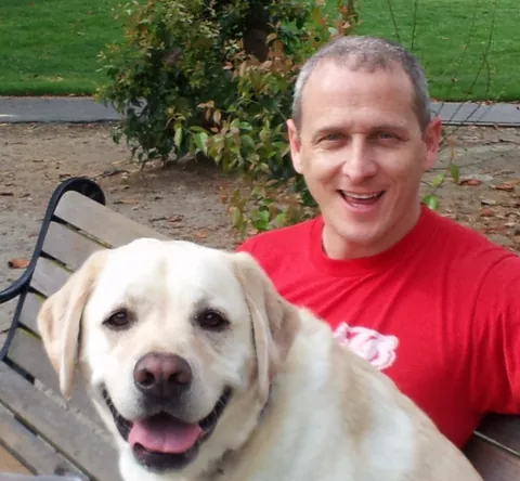 Mike Somlo sitting on a park bench with a yellow Labrador